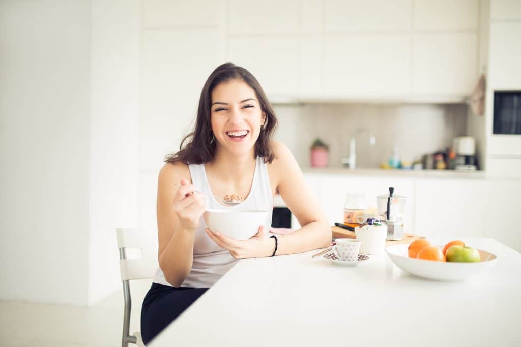 Young smiling woman eating cereal and smiling.Healthy breakfast.Starting your day.Dieting,fitness and wellbeing.Positive energy and emotion.Productivity,happiness,enjoyment concept.Morning ritual